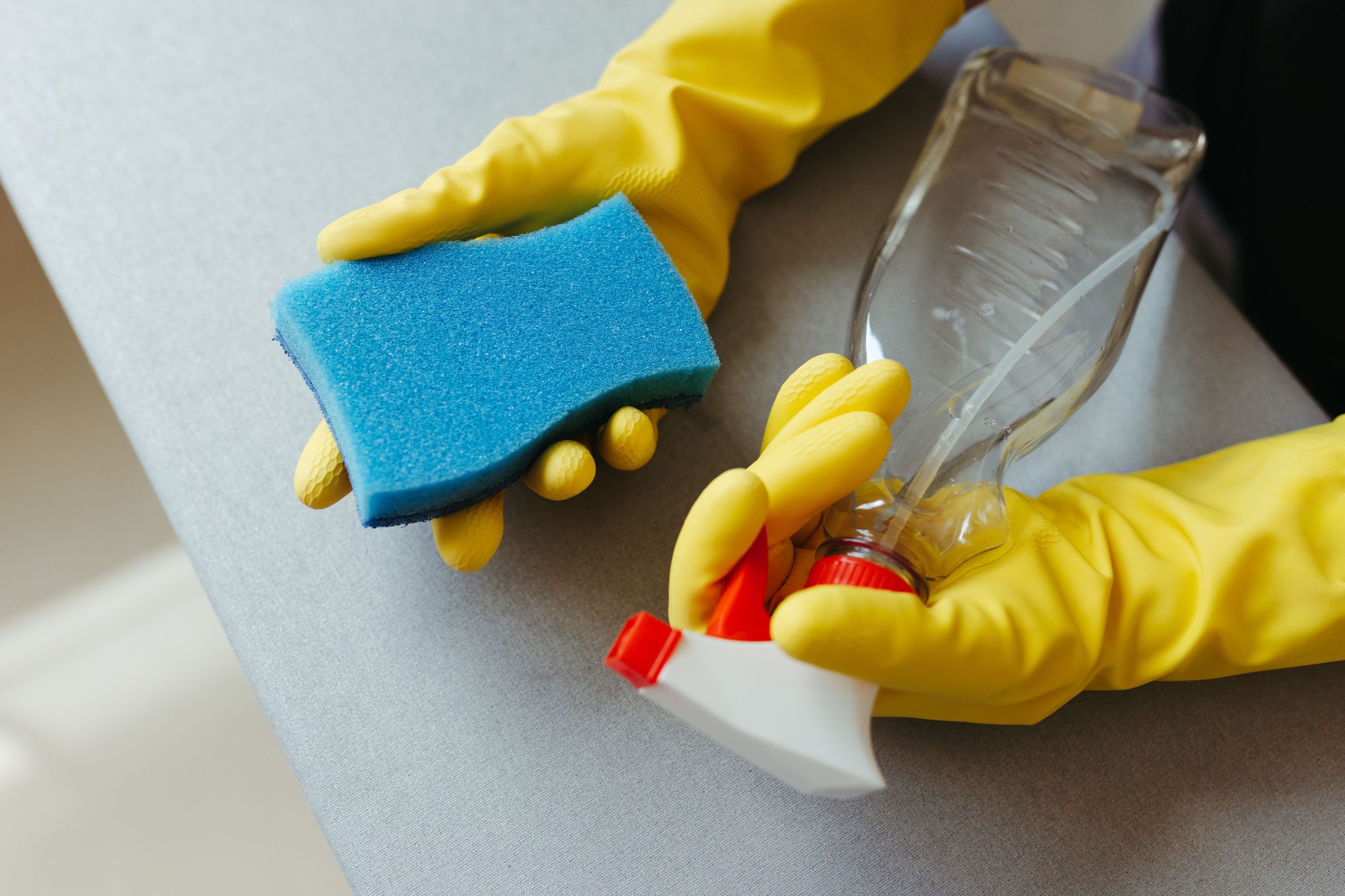 Mains gantées tenant éponge et spray nettoyant